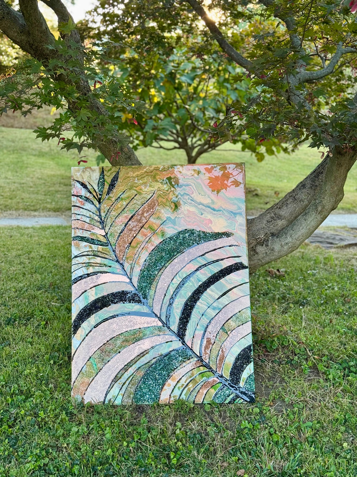 Colorful abstract leaf painting and resin art on grass with trees in the background