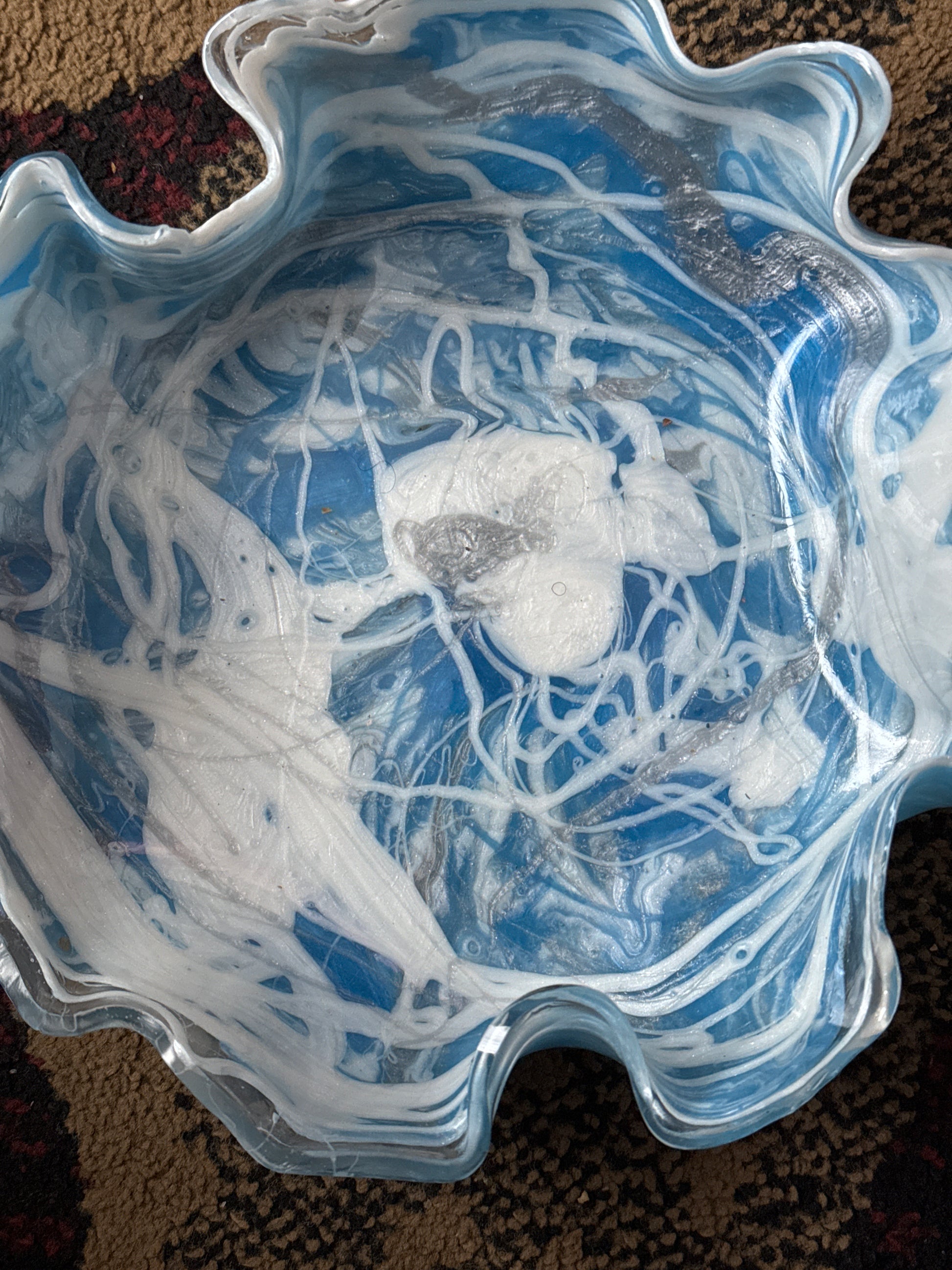 A handcrafted, multicolored resin artisan bowl with a free-formed shape displayed on a white furry surface.