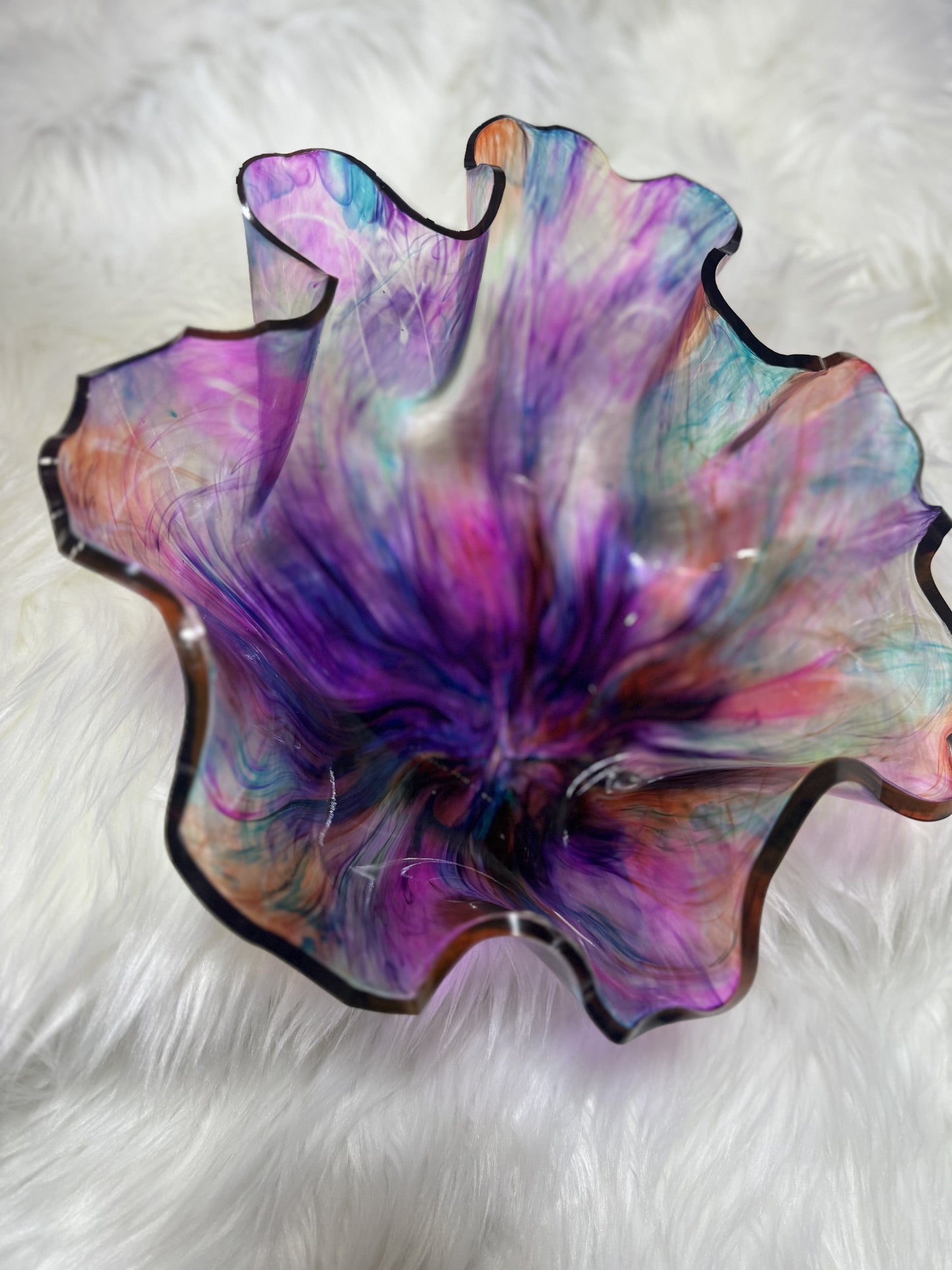 A handcrafted, multicolored resin artisan bowl with a free-formed shape displayed on a white furry surface.