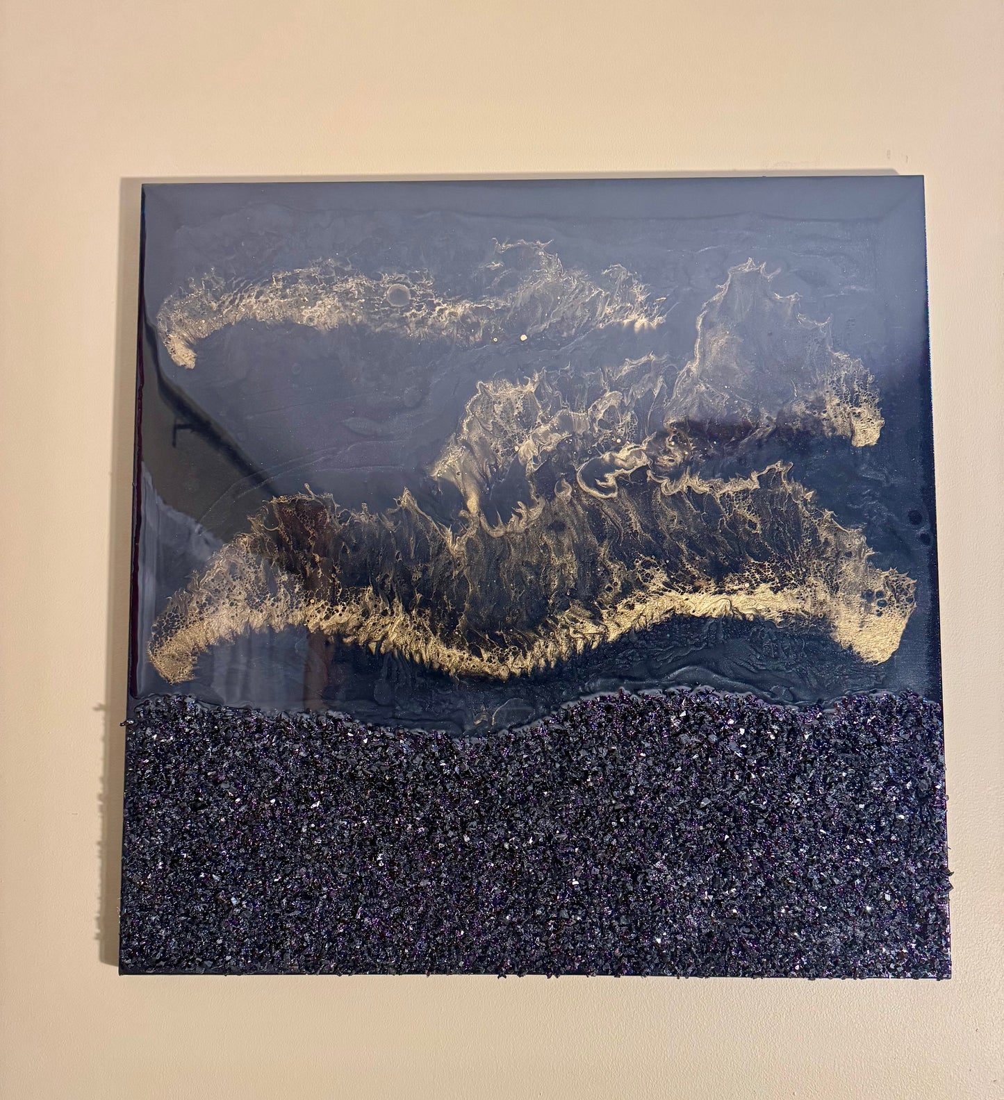 Abstract art piece with gold and black patterns on a beige wall