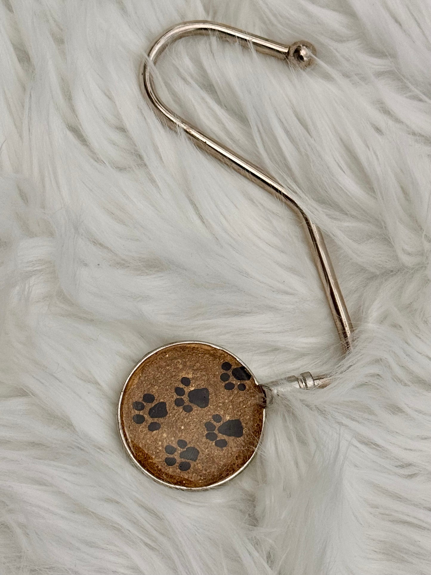 A silver-toned metal purse holder featuring a brown glittery background and black paw print patterns, displayed on a white faux fur surface.