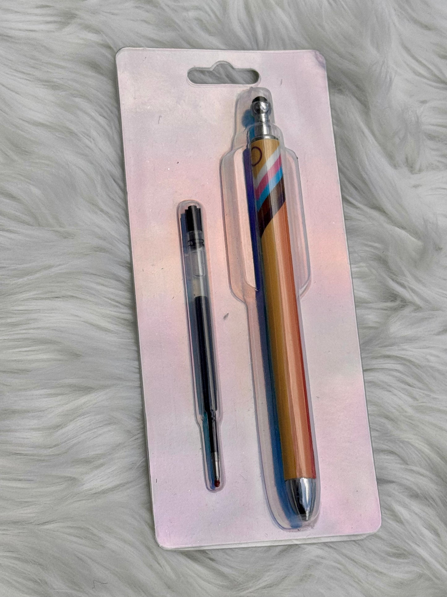 A stylus pen and its refill cartridge in blister packaging, placed on a white faux fur surface. The stylus has a metallic gold body with blue, pink, and purple diagonal stripes, and silver metal tips.