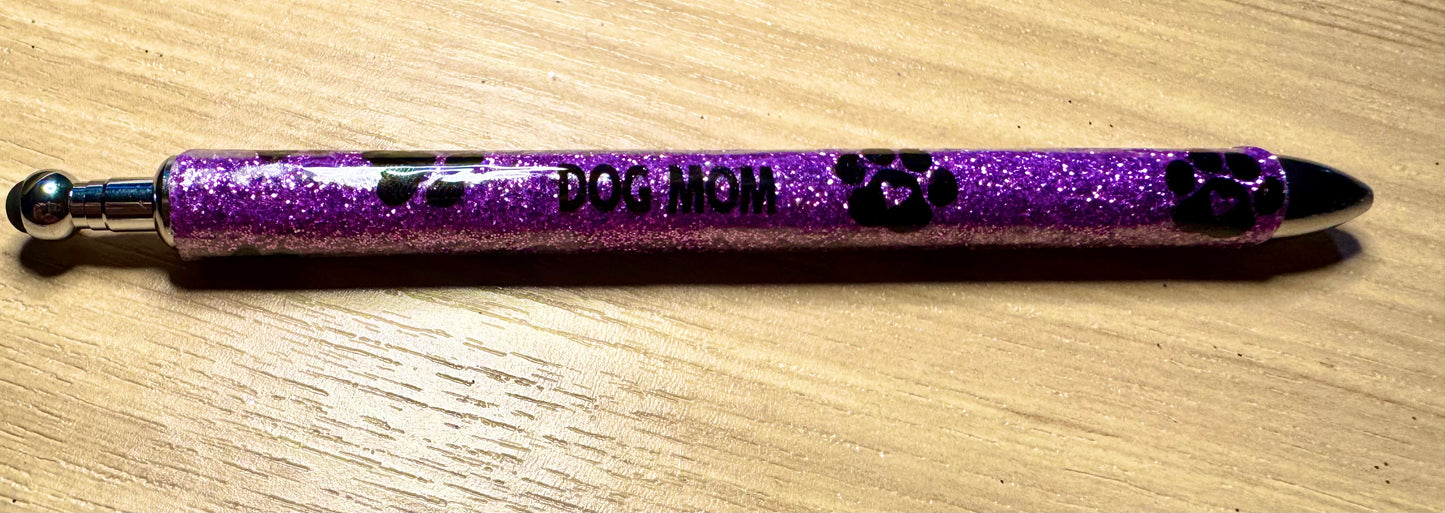 Purple glittery pen with 'DOG MOM' text on a wooden surface