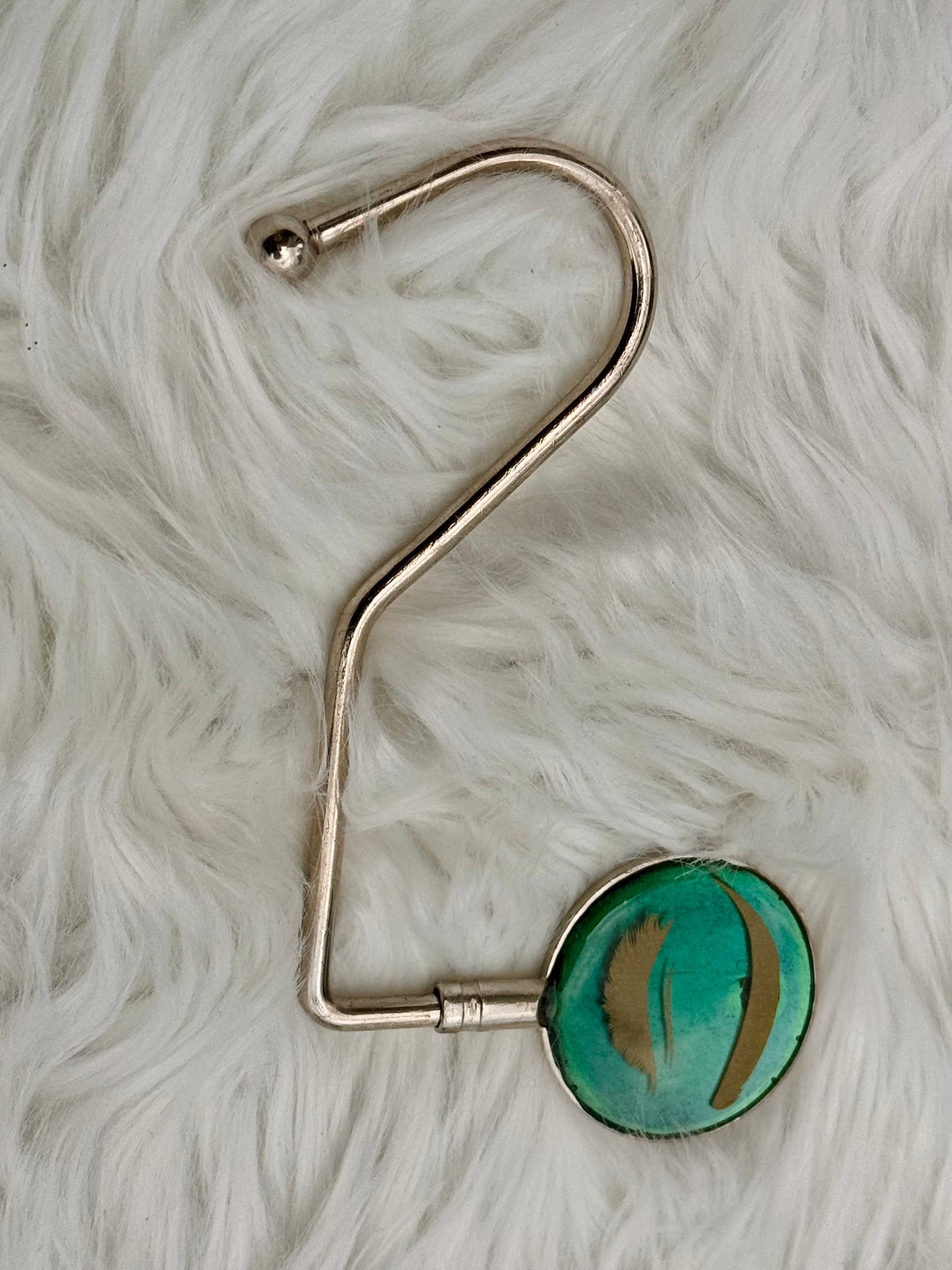 A silver metal hook purse holder with a emerald background and golden eyes