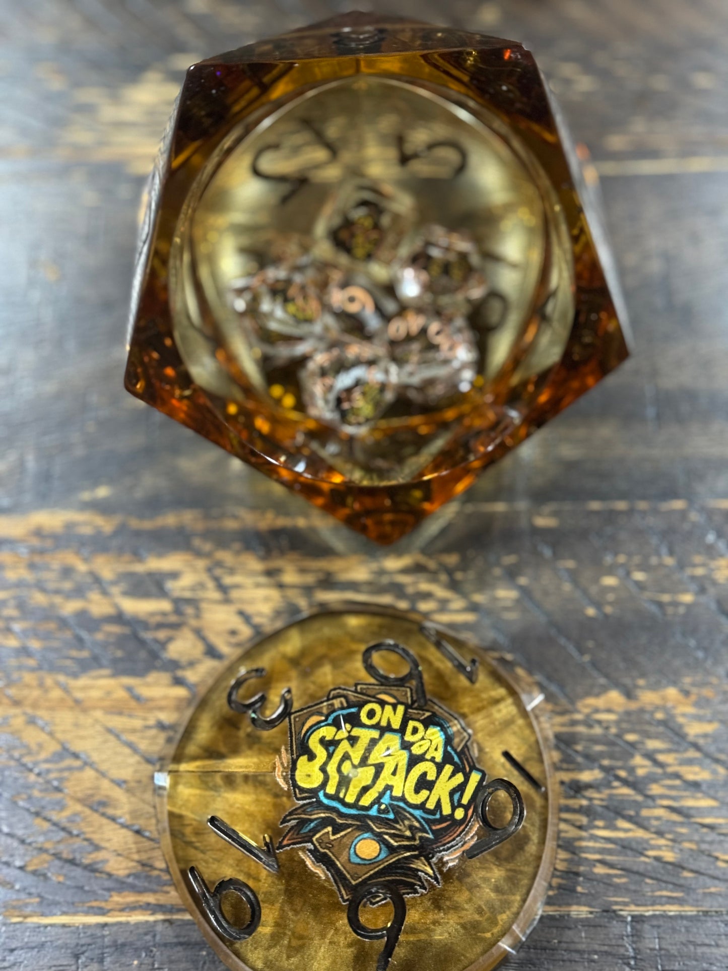 Hexagonal die with a clear face showing mechanical components, and a metallic base with 'On da Stack!' text.