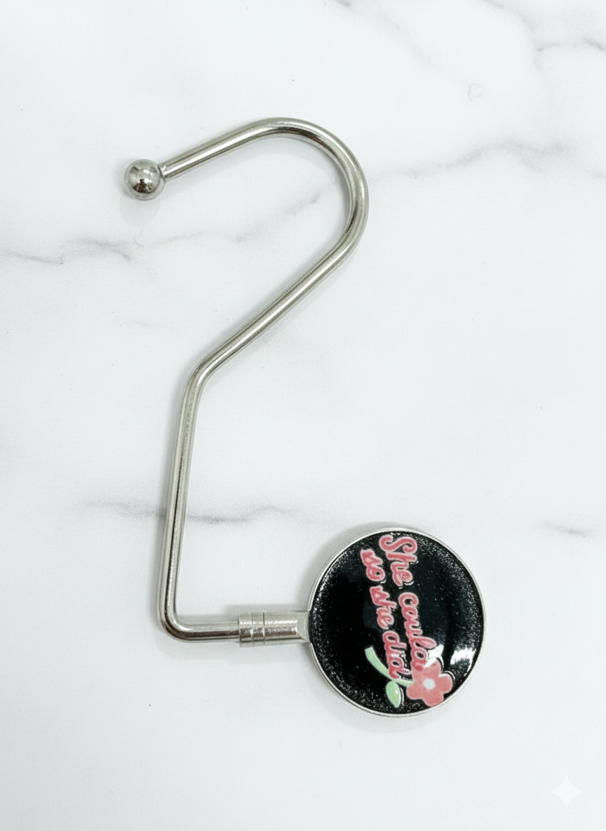 Metal bag hanger with a black circular tag on a white marble background