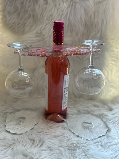 A red wine caddy made of resin, designed to hold a wine bottle and two wine glasses, displayed on a white furry surface.